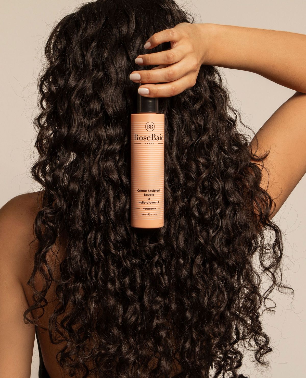 Woman with long dark curls holding a hair product