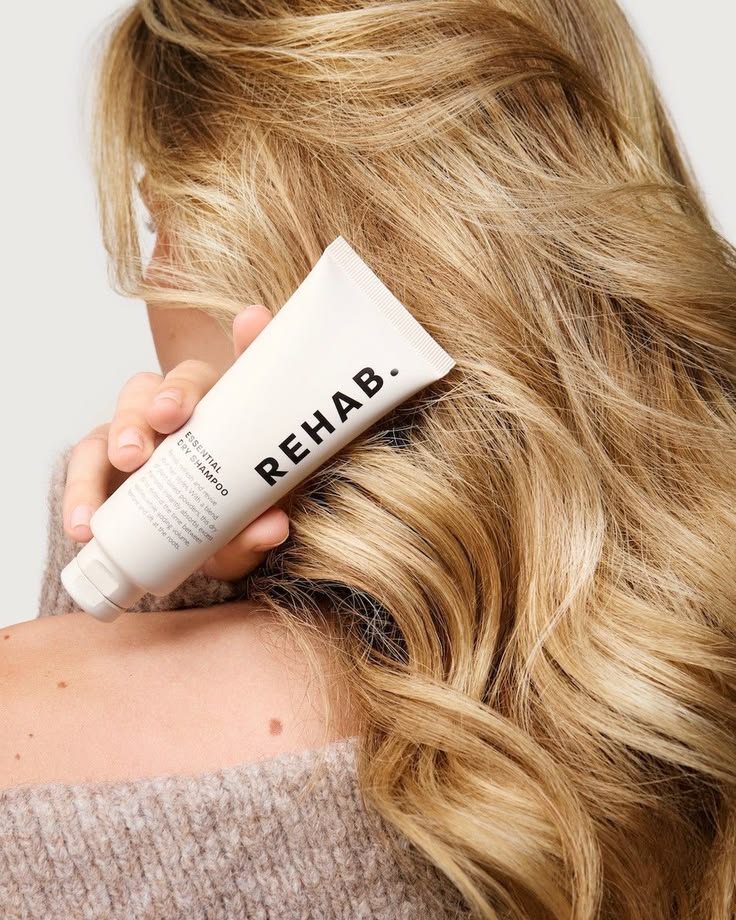 Woman with wavy blonde hair holding a tube of hair product