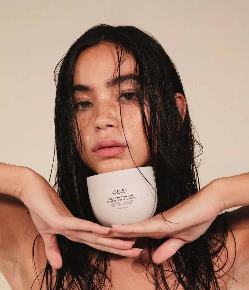 Woman with wet dark hair holding a hair mask